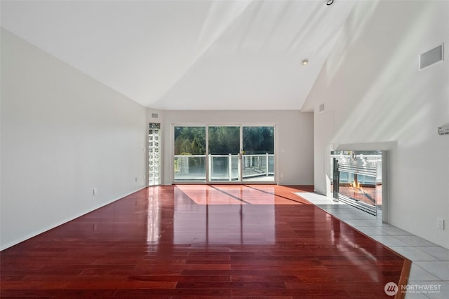 unfurnished living room featuring visible vents, high vaulted ceiling, wood finished floors, and a tiled fireplace