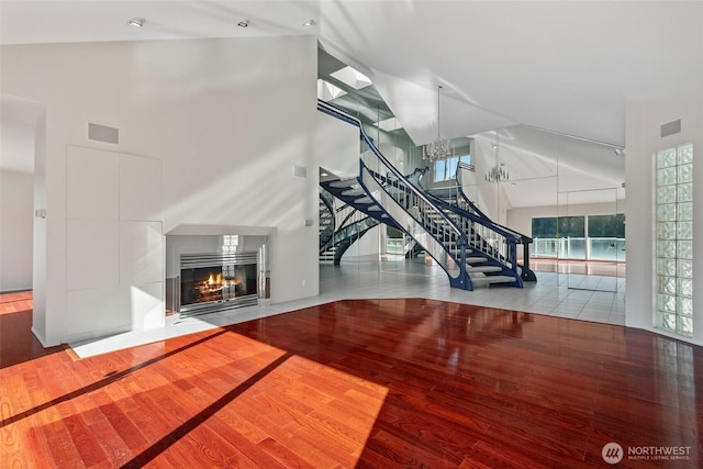 living area featuring wood finished floors, visible vents, high vaulted ceiling, a fireplace with flush hearth, and stairs