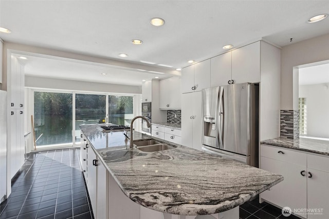 kitchen with a sink, an island with sink, white cabinets, stainless steel appliances, and dark tile patterned flooring