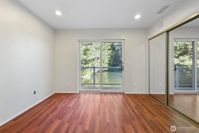 unfurnished bedroom with visible vents, wood finished floors, baseboards, and access to outside