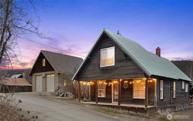 view of front of house featuring a chimney, covered porch, metal roof, and a garage