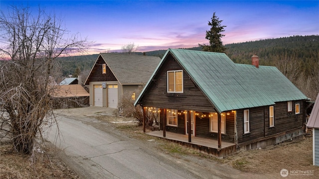 chalet / cabin featuring an outbuilding, driveway, covered porch, metal roof, and a chimney