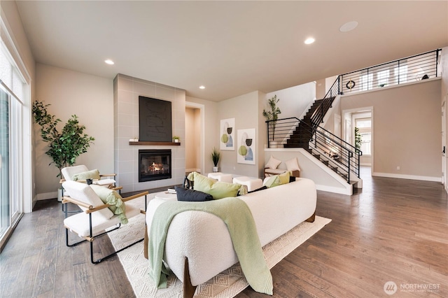 living area featuring a tiled fireplace, stairway, wood finished floors, and baseboards