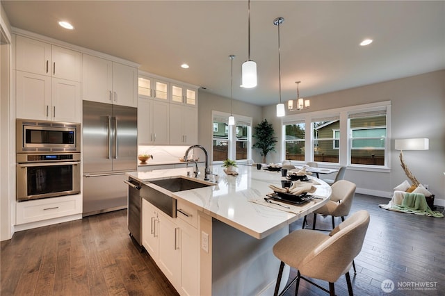 kitchen with light stone counters, a sink, decorative backsplash, white cabinets, and built in appliances