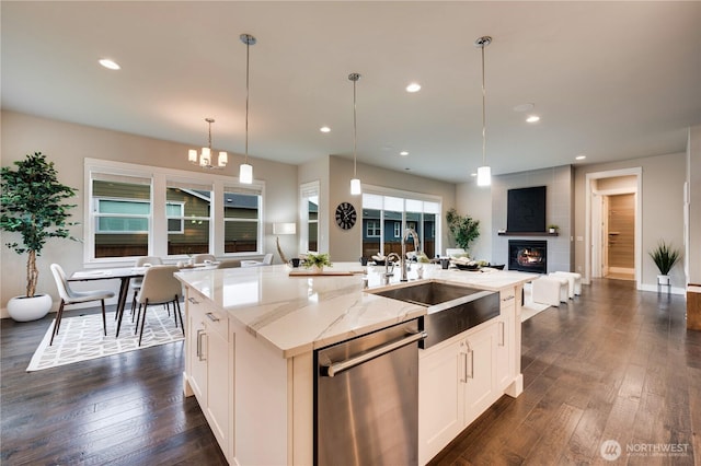 kitchen with open floor plan, dishwasher, an island with sink, light stone counters, and a sink