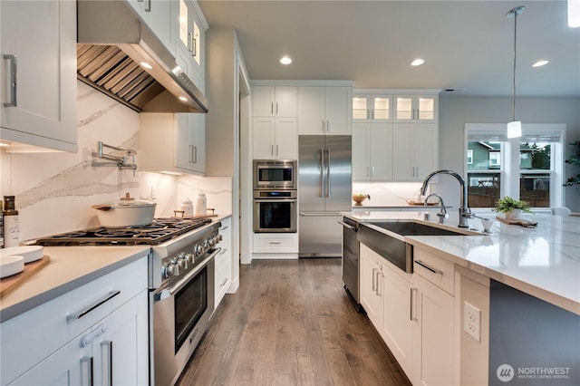 kitchen featuring dark wood-style floors, a sink, built in appliances, under cabinet range hood, and decorative light fixtures