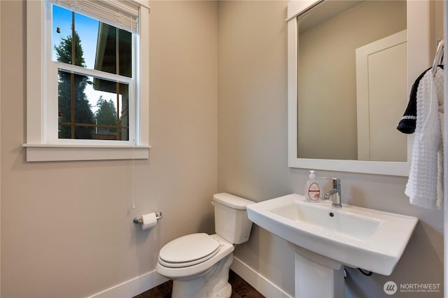 half bathroom with toilet, baseboards, and a sink