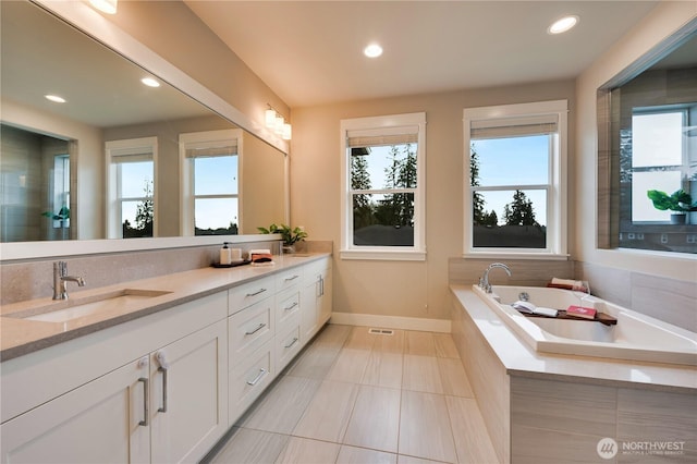 full bath featuring baseboards, a garden tub, double vanity, recessed lighting, and a sink