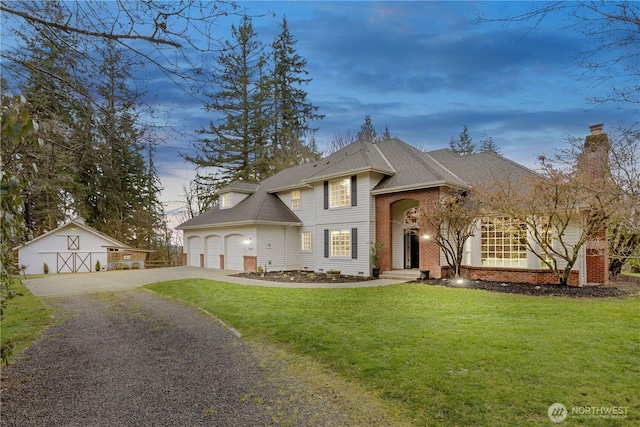 view of front of home with brick siding, an attached garage, a front yard, an outbuilding, and driveway