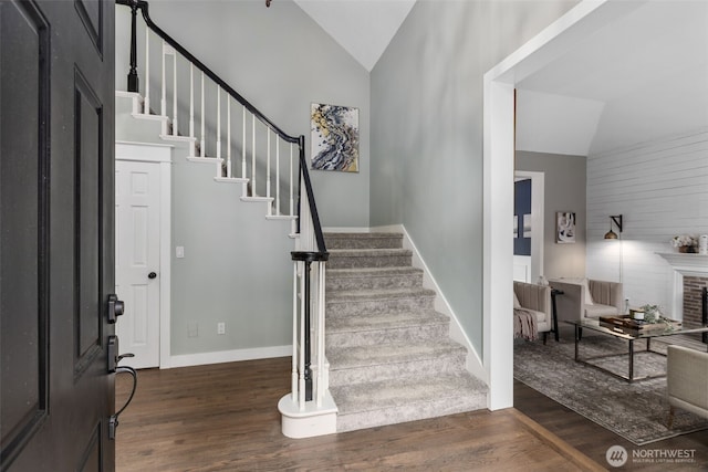 foyer entrance with baseboards, stairs, dark wood-type flooring, vaulted ceiling, and a brick fireplace