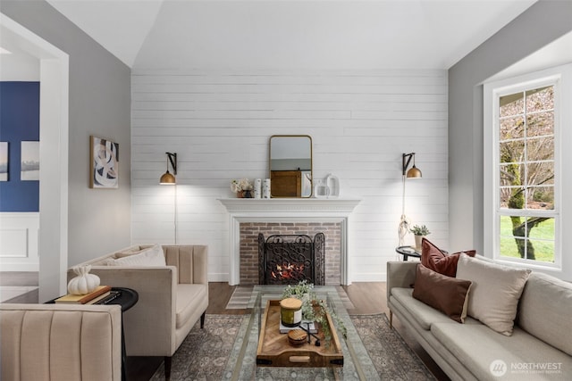 living area featuring vaulted ceiling, a brick fireplace, and wood finished floors