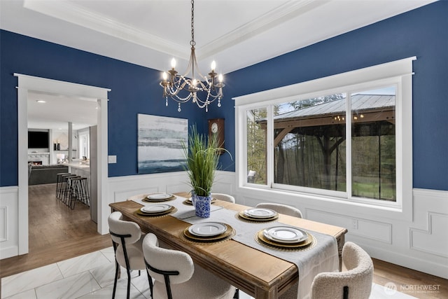 dining space with a lit fireplace, a tray ceiling, a chandelier, and wainscoting