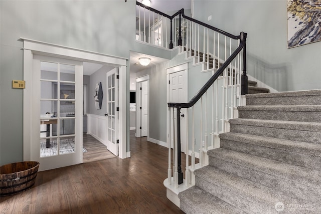 staircase with wood finished floors, baseboards, and a towering ceiling