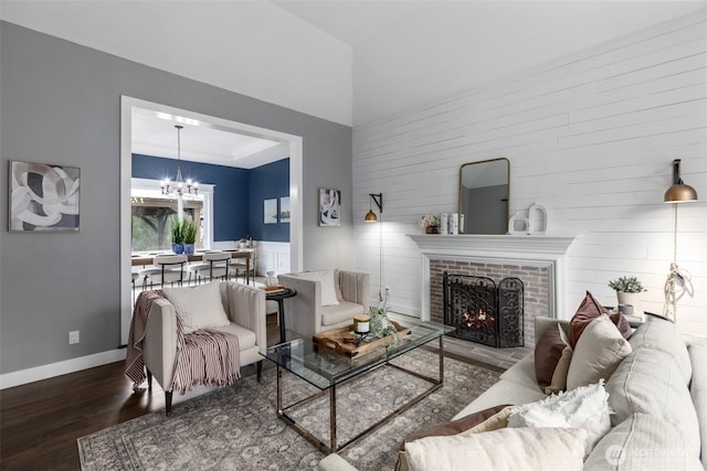 living area featuring a raised ceiling, wood finished floors, a fireplace, baseboards, and a chandelier