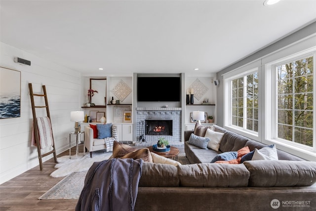 living room with a brick fireplace, recessed lighting, wood finished floors, and wooden walls