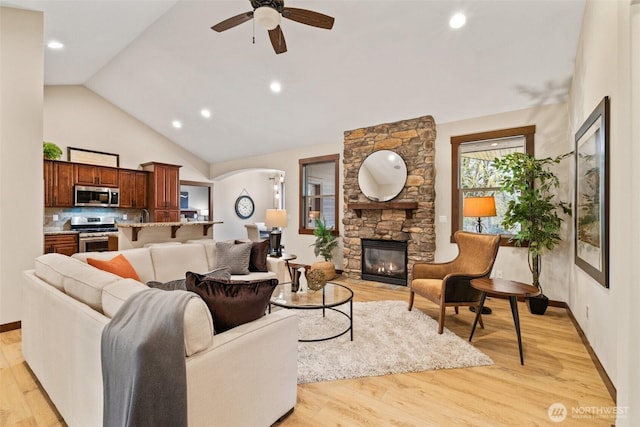 living room featuring light wood finished floors, a fireplace, a ceiling fan, and arched walkways