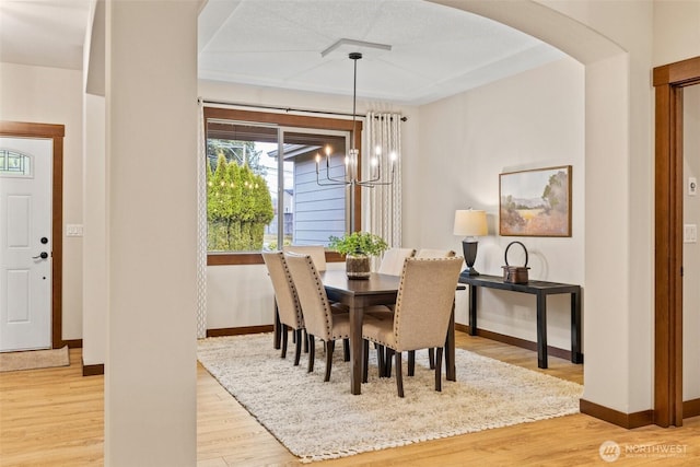 dining area featuring an inviting chandelier, light wood-style floors, arched walkways, and baseboards