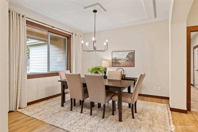 dining space with baseboards, arched walkways, an inviting chandelier, and wood finished floors