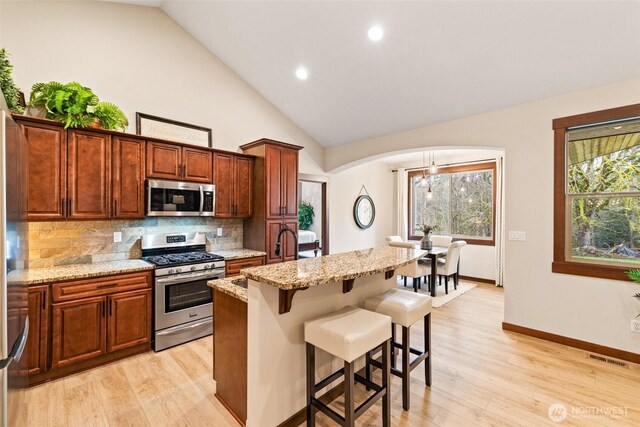 kitchen with a breakfast bar area, light stone countertops, light wood finished floors, decorative backsplash, and appliances with stainless steel finishes