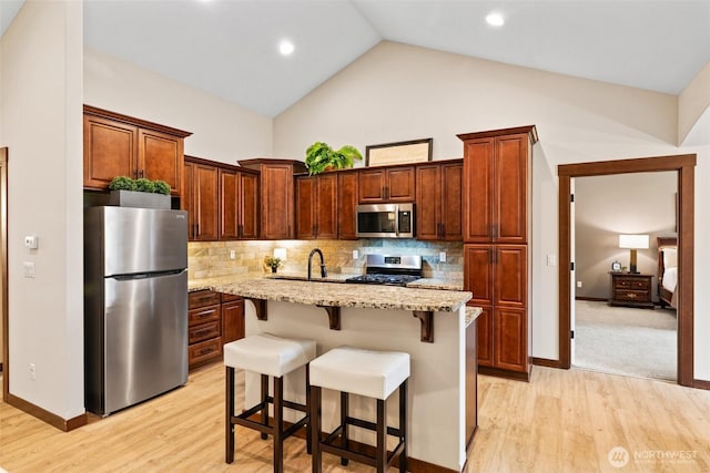 kitchen featuring light stone countertops, light wood-type flooring, decorative backsplash, appliances with stainless steel finishes, and a kitchen breakfast bar