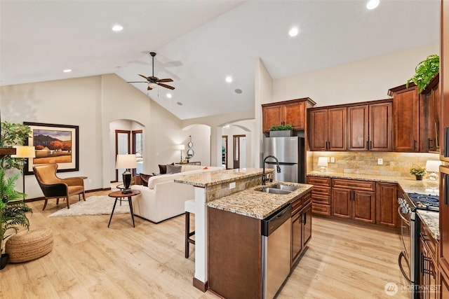 kitchen featuring a kitchen island with sink, arched walkways, a sink, stainless steel appliances, and open floor plan