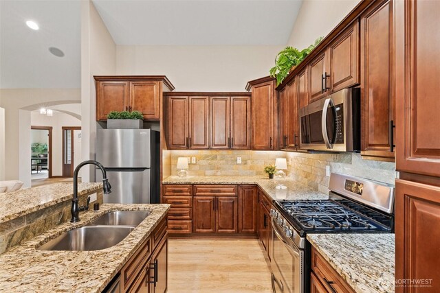 kitchen featuring light wood finished floors, tasteful backsplash, light stone counters, stainless steel appliances, and a sink