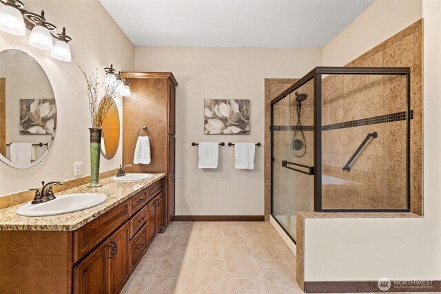 bathroom featuring a shower stall, double vanity, baseboards, and a sink