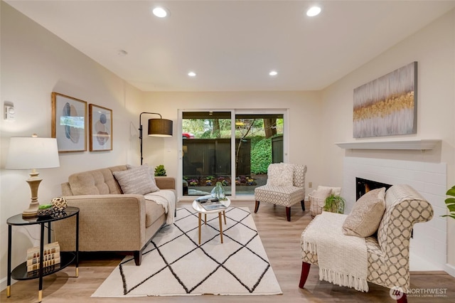 living room featuring recessed lighting, wood finished floors, and a warm lit fireplace