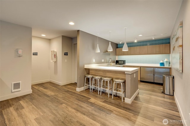 kitchen featuring a breakfast bar area, visible vents, a peninsula, light countertops, and black microwave