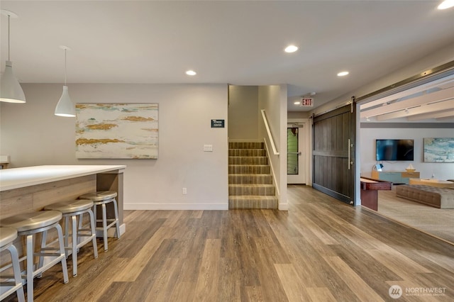 kitchen featuring a kitchen breakfast bar, wood finished floors, recessed lighting, a barn door, and dark brown cabinets