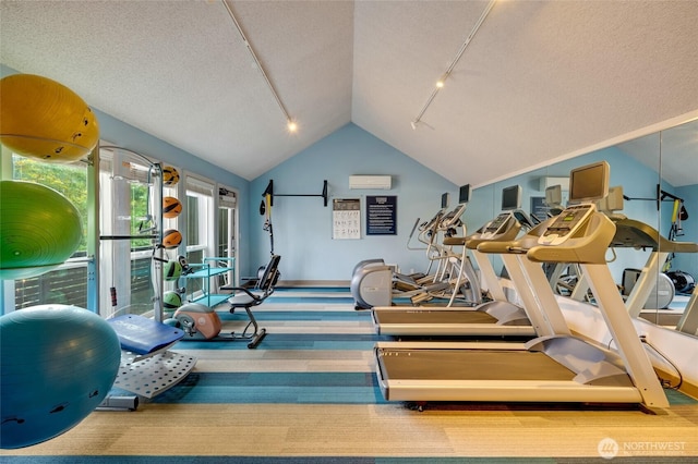 gym with a wall mounted air conditioner, track lighting, a textured ceiling, carpet flooring, and vaulted ceiling