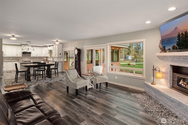 living area featuring recessed lighting, baseboards, a brick fireplace, and dark wood-style floors