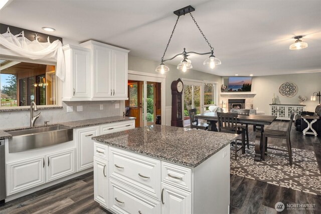 kitchen featuring dark wood-style floors, a brick fireplace, a center island, and a sink