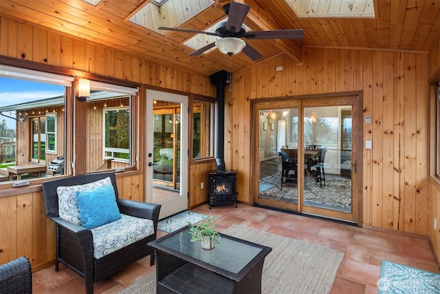 interior space featuring wooden walls, vaulted ceiling with skylight, wooden ceiling, and a wood stove