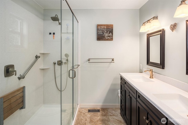 bathroom with a sink, baseboards, a stall shower, and double vanity