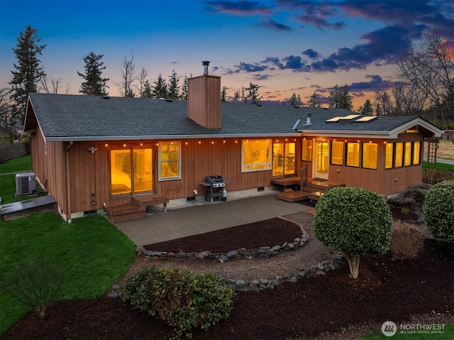 back of property featuring central air condition unit, a shingled roof, crawl space, a chimney, and a patio area