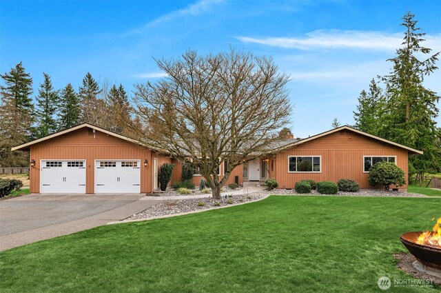 single story home with aphalt driveway, a garage, a fire pit, and a front lawn