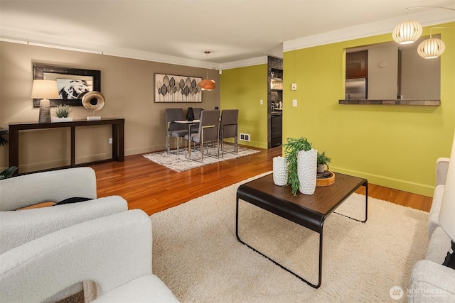 living area featuring visible vents, baseboards, wood finished floors, and crown molding