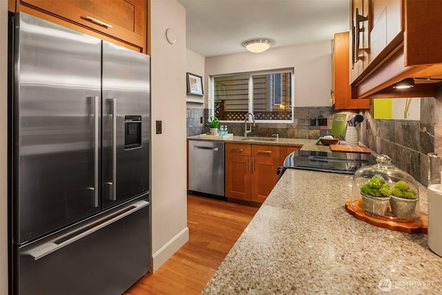 kitchen with brown cabinetry, light wood finished floors, a sink, decorative backsplash, and stainless steel appliances