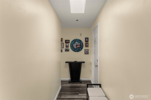 hallway featuring a skylight, baseboards, and dark wood-style floors