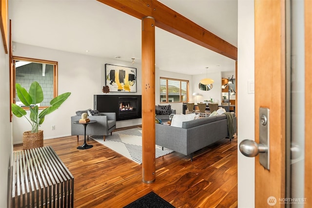 living area with a glass covered fireplace, beam ceiling, and wood finished floors