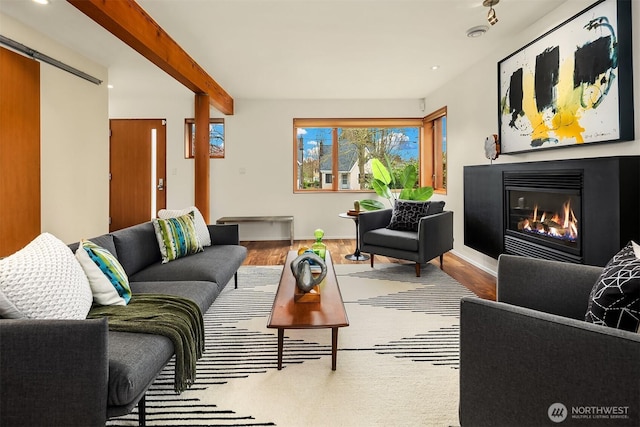 living room with wood finished floors, baseboards, beam ceiling, and a glass covered fireplace