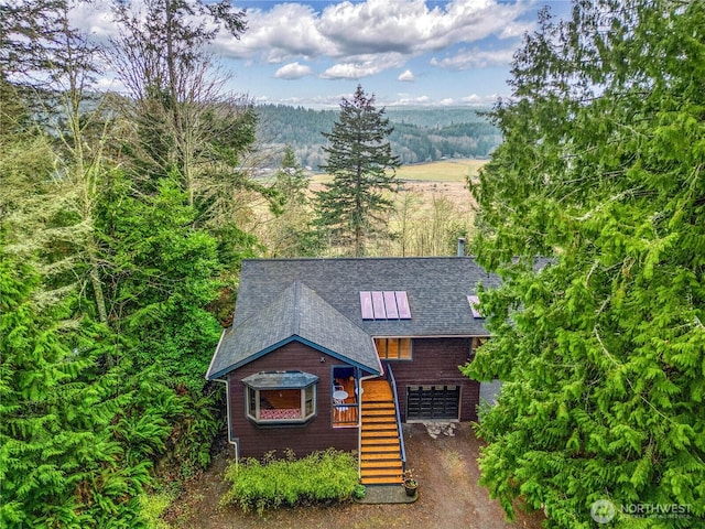 chalet / cabin featuring a forest view, a shingled roof, a garage, brick siding, and stairs