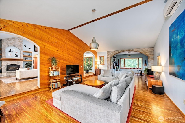 living area featuring an AC wall unit, wood finished floors, arched walkways, a stone fireplace, and wood walls