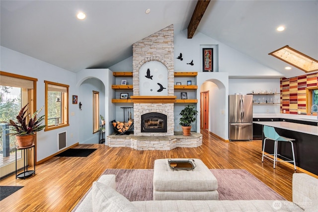 living room featuring high vaulted ceiling, beam ceiling, arched walkways, a stone fireplace, and light wood-type flooring