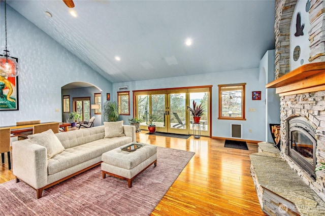 living room with high vaulted ceiling, arched walkways, a fireplace, light wood finished floors, and baseboards