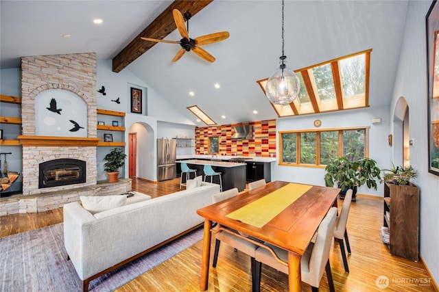 living area with high vaulted ceiling, a fireplace, arched walkways, beamed ceiling, and light wood-type flooring