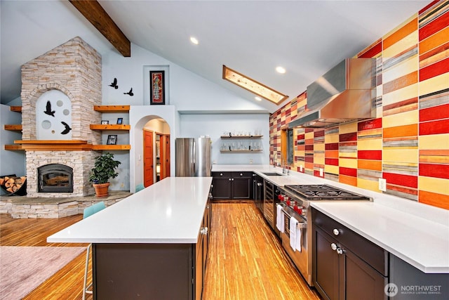 kitchen with open shelves, a kitchen island, wall chimney range hood, appliances with stainless steel finishes, and a sink