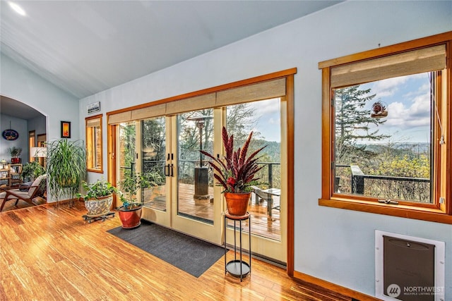 doorway to outside with lofted ceiling, wood finished floors, arched walkways, and french doors