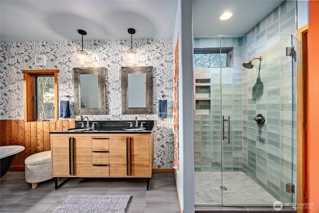 bathroom featuring tile patterned floors, a sink, a shower stall, wallpapered walls, and double vanity